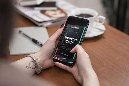 Person holding a smartphone with 'Beacon Code' course on a table with coffee and magazine.