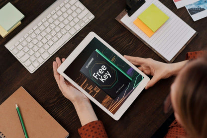 Person using a tablet on a desk with a keyboard and stationery items.